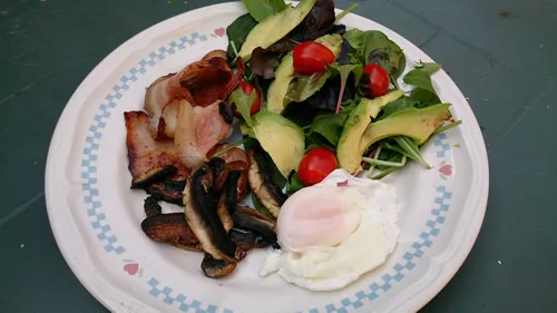 A plate of salad, bacon, mushrooms and a poached egg