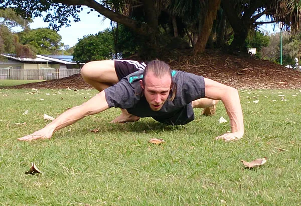 A man stretching in a low lunge on the grass in a park
