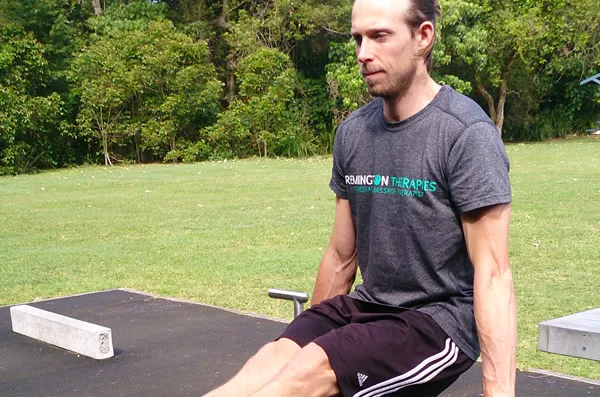 A man sitting on a mat in a park, stretching