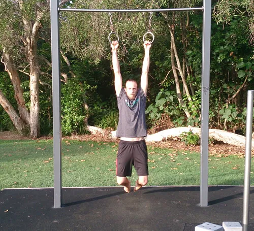 A man hanging from gymnastic rings on an outdoor bar