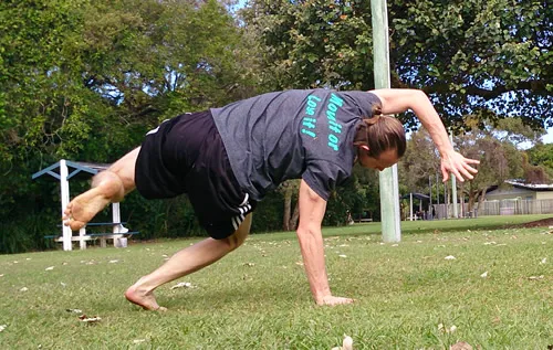 Someone moving on all fours in a crab position on the grass in a park